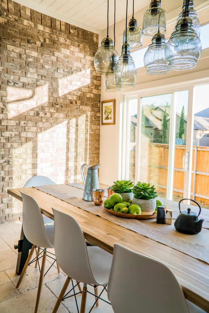 Home Sunlit dining room with contemporary decor and a rustic brick wall, featuring stylish lighting and a wooden table.